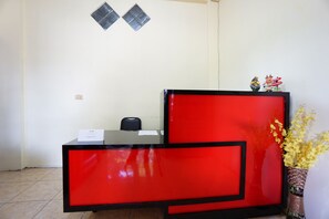 A reception desk with a red and black design, a small chair, and a vase with yellow flowers. - OYO 1912 Kengkang Residence (Manado)