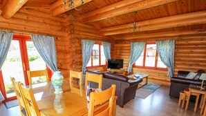 A log cabin interior with a dining area, sofa, TV, and a fireplace. - Yew Lodge (Oakham)