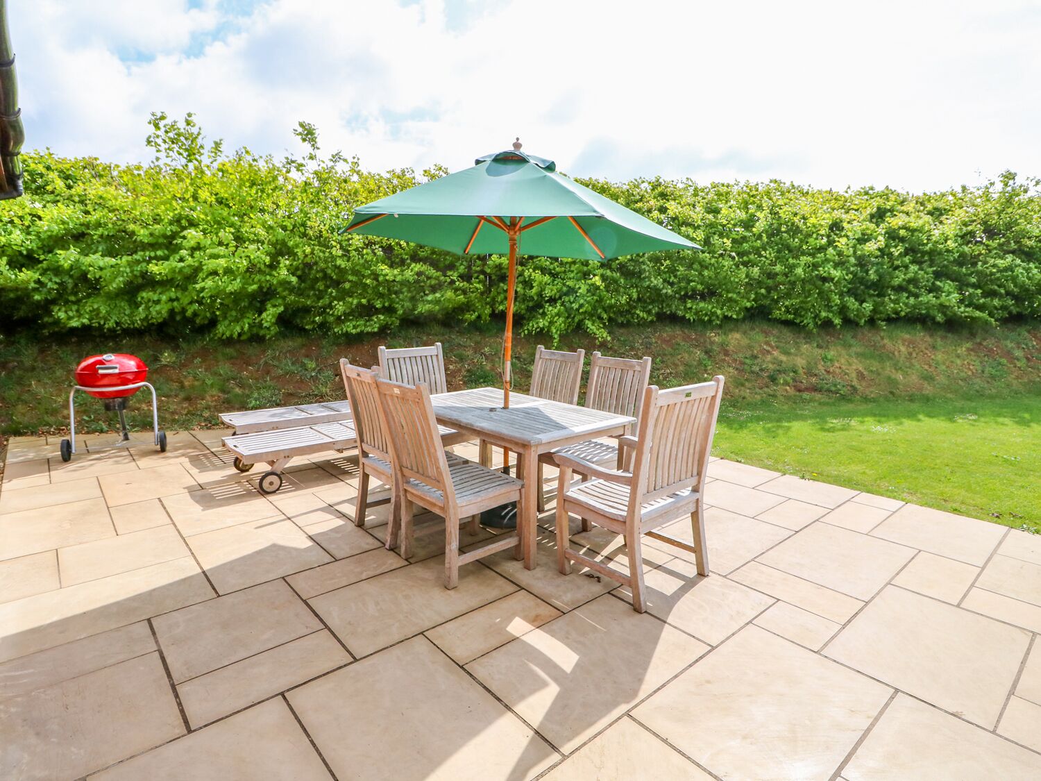 A patio with a table and chairs, a grill, and a green umbrella.