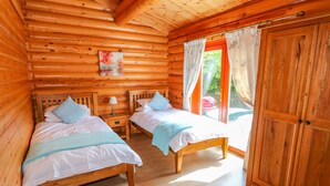 A log cabin bedroom with two wooden beds, a nightstand, a painting, and a sliding door to a balcony. - Yew Lodge (Oakham)