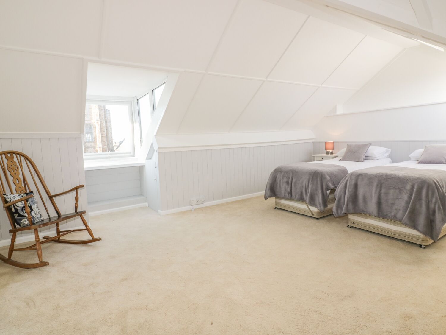 A bedroom with two beds, a rocking chair, and a window.