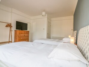 Quarto com uma cama grande, penteadeira de madeira, televisão na parede e porta que dá para outro cômodo.