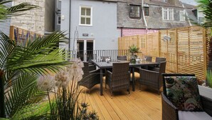 A patio area with a wooden deck, wicker furniture, and potted plants. - Harbourside House (Weymouth)