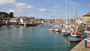 A harbor with boats docked, buildings along the waterfront, and a clear sky. - Harbourside House (Weymouth)
