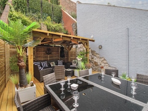 An outdoor patio with a wooden pergola, wicker furniture, and a glass-top table with wine glasses. - Harbourside House (Weymouth)