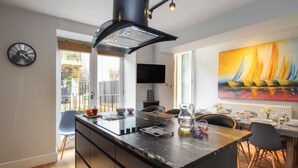A modern kitchen with a central island, a dining area with a table set for four, and a large window with a view of the outdoors. - Harbourside House (Weymouth)