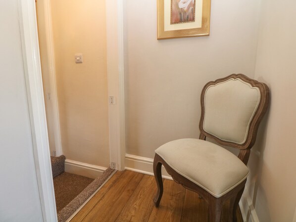 A hallway with a wooden chair, a carpeted area, and a framed picture on the wall.