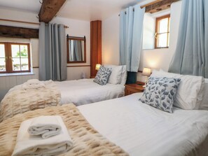 A hotel room with two beds, a wooden headboard, a mirror, and a window with curtains. - Slade Cottage (Ashbourne)