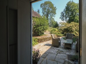 A stone patio with wicker furniture, a stone wall, and a view of trees and a building. - Slade Cottage (Ashbourne)
