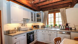 Una cocina con armarios blancos, piso de ladrillo y techo de madera.