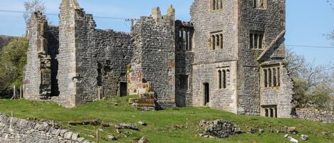 A historic stone building with multiple towers and arched windows, surrounded by a stone wall and grassy area.