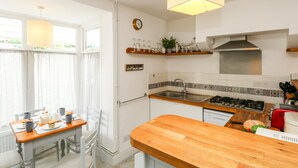 A modern kitchen with a wooden countertop, a gas stove, and a sink. There is a dining area with a table and chairs. - Harbour Catch Cottage (Weymouth)