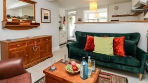 A living room with a green sofa, wooden cabinet, and a coffee table with fruits and bottles. - Harbour Catch Cottage (Weymouth)