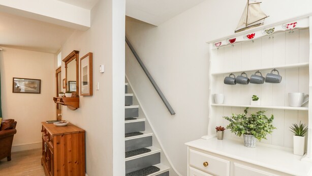 A staircase with a gray handrail and white walls, leading to a landing with a wooden bench and a small table. - Harbour Catch Cottage (Weymouth)