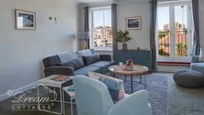 Un salon moderne avec un canapé gris, une table basse ronde et une vue sur les immeubles à travers de grandes fenêtres.
