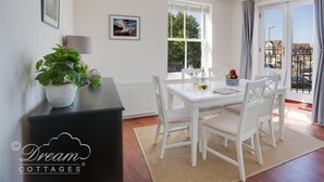 Un coin repas avec une table et des chaises blanches, une plante en pot et une fenêtre donnant sur l’extérieur.