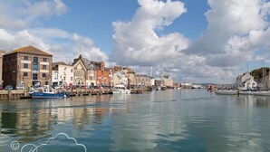 Une ville côtière dotée de bâtiments historiques, d’un port de plaisance où sont amarrés des bateaux et d’un ciel dégagé.
