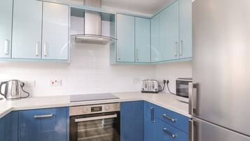A modern kitchen with blue cabinets, a stainless steel refrigerator, a built-in oven, and a toaster.