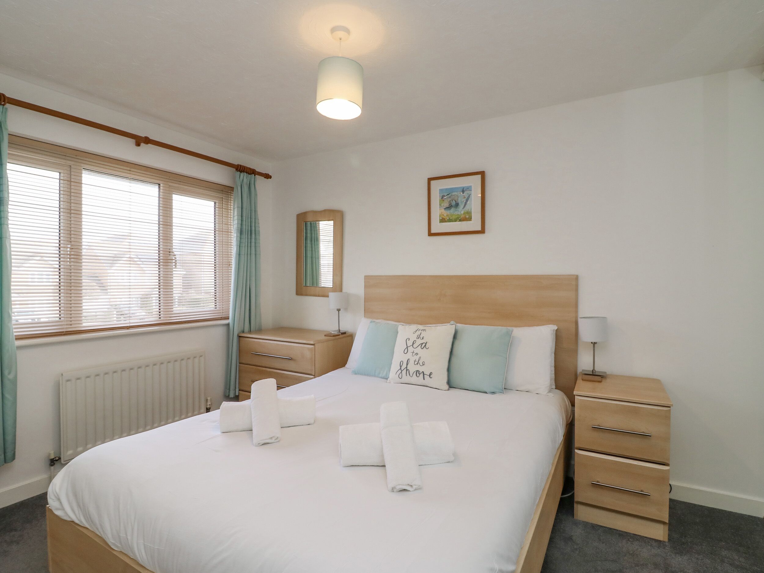 A hotel room with a bed, bedside tables, a radiator, a window with curtains, and a wall-mounted picture.