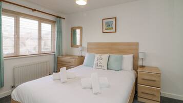 A hotel room with a bed, bedside tables, a radiator, a window with curtains, and a wall-mounted picture.