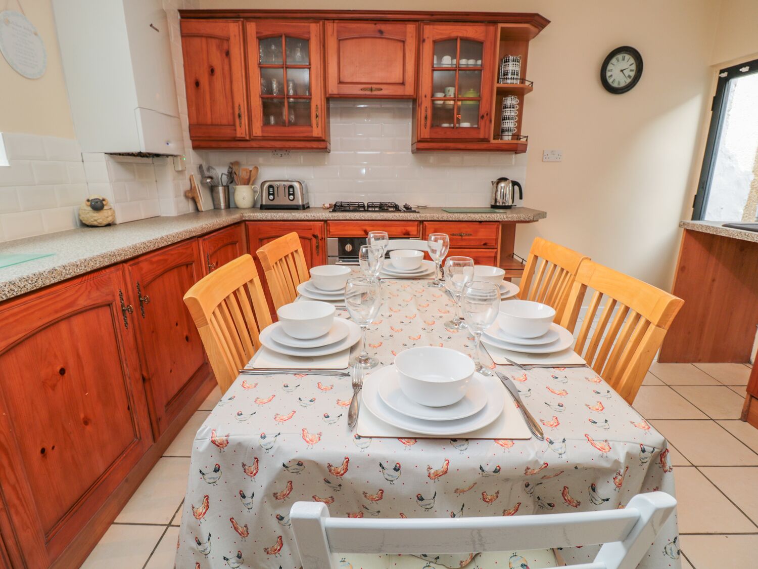Una cocina con armarios de madera, una mesa de comedor preparada para seis personas y un reloj en la pared.