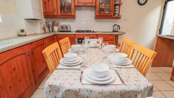 Una cocina con armarios de madera, una mesa de comedor preparada para seis personas y un reloj en la pared.