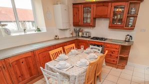 Una cocina con armarios de madera, una mesa de comedor preparada para seis personas y una ventana con vista a un edificio de tejados rojos.