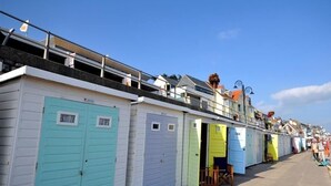 Une rangée de cabanes de plage colorées, aux portes fermées, un chemin piétonnier en béton et un ciel bleu azur.