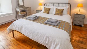 Een keurig opgemaakte slaapkamer met een bed, twee nachtkastjes met lampen, een kaptafel en een spiegel.