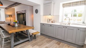 Een moderne keuken met grijze kastjes, een houten eettafel en een inbouwoven.