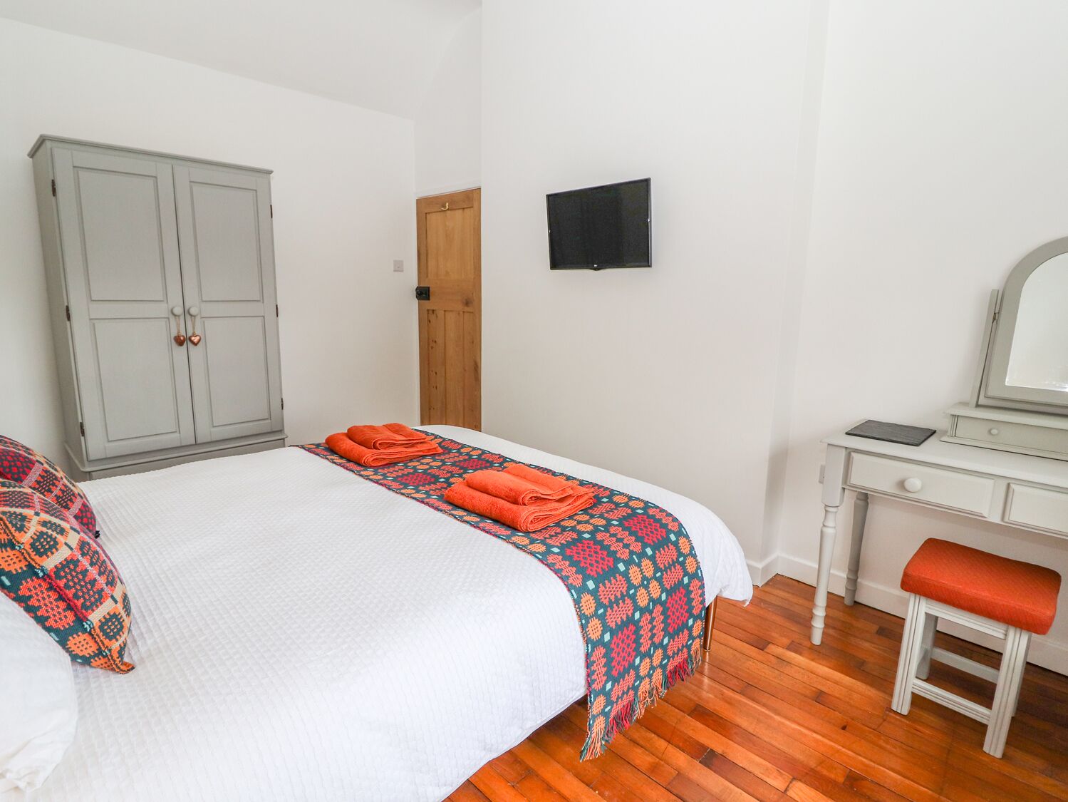 A bedroom with a bed, a wardrobe, a desk, a chair, and a television on the wall.