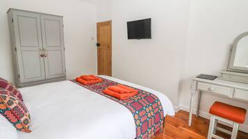 A bedroom with a bed, a wardrobe, a desk, a chair, and a television on the wall.