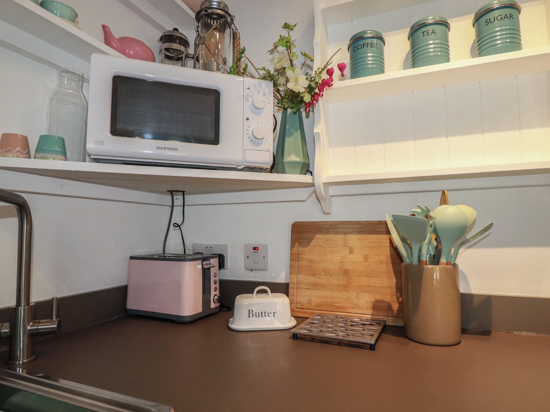 Una cucina con forno a microonde, tostapane, tagliere, contenitore per burro e un vaso con fiori.