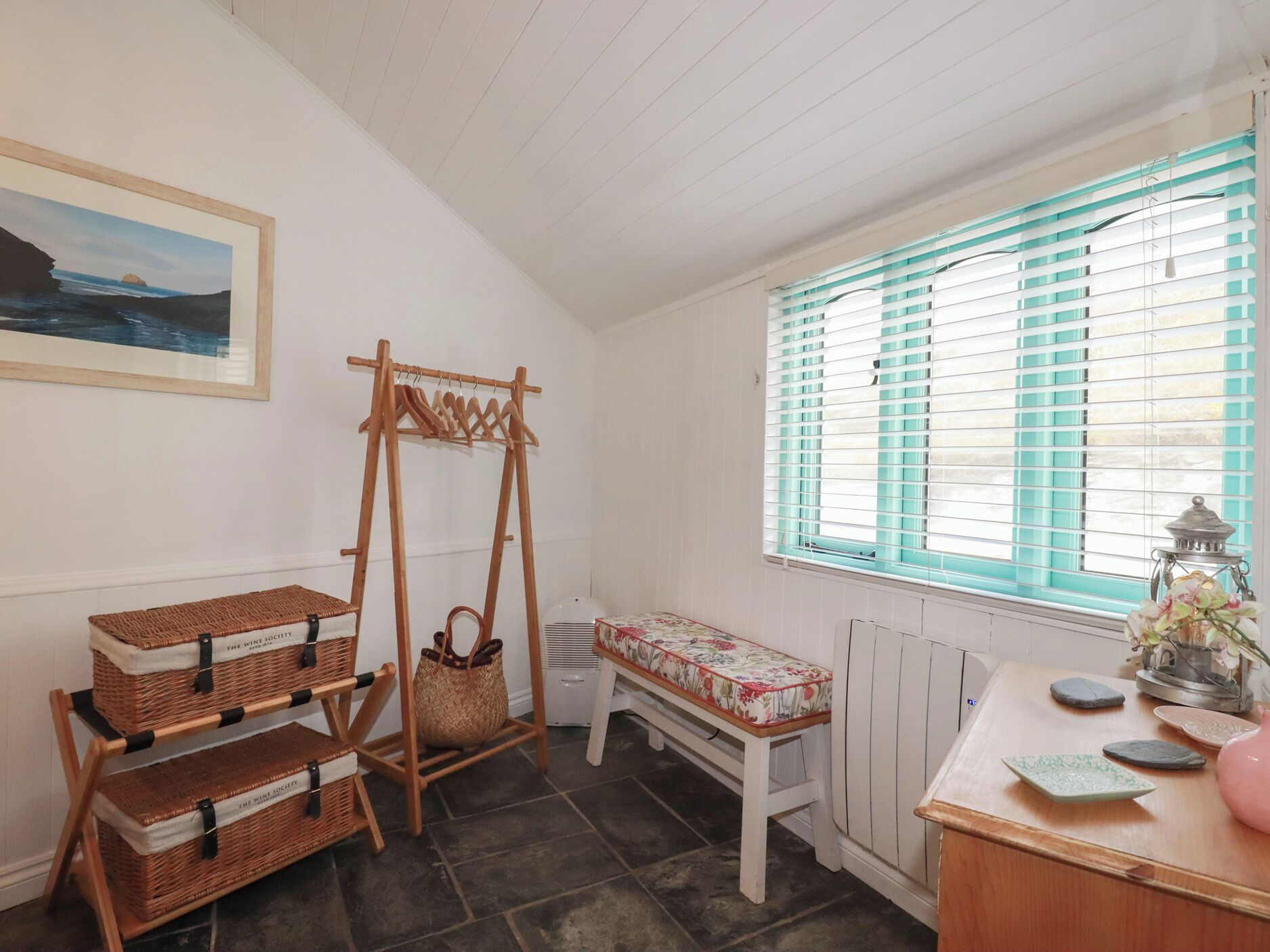 A room with a wooden bench, a wicker shelf unit, a radiator, and a window with blinds.