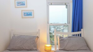 Et værelse med to senge, et vindue med blå gardiner og en lampe på sengebordet.