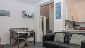 En moderne stue med spiseplads, en sort lædersofa og en trappe til øvre etage.