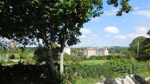 Un mur de pierre avec un bâtiment en pierre en arrière-plan, entouré de verdure et sous un ciel dégagé.