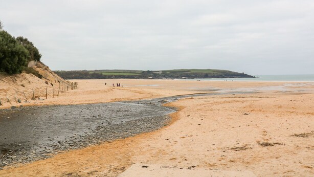 A beach with a sandy shore, a grassy hill in the background, and a few people walking. - Tynk (Padstow)