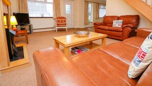 A living room with a sofa, a coffee table, a television, and a fireplace. - Tynk (Padstow)