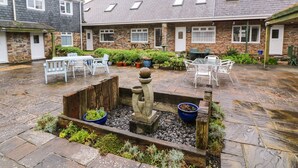 A courtyard with stone flooring, white outdoor furniture, and a central planter with plants. - Tynk (Padstow)