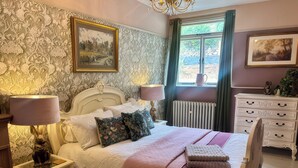 Ein Schlafzimmer mit Bett, Nachttischen, einem Schminktisch und einem Fenster mit Vorhängen.