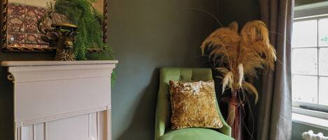 A room with a green upholstered chair, a white fireplace, and a mirror with a floral pattern.