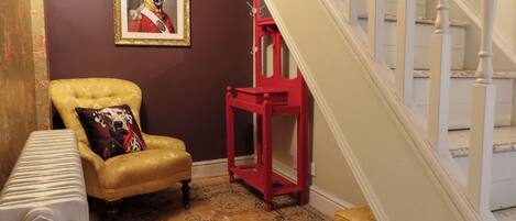 Una habitación con alfombra estampada, un sillón amarillo con un cojín de lunares de perro dálmata, una mesita auxiliar roja y un cuadro enmarcado en la pared.