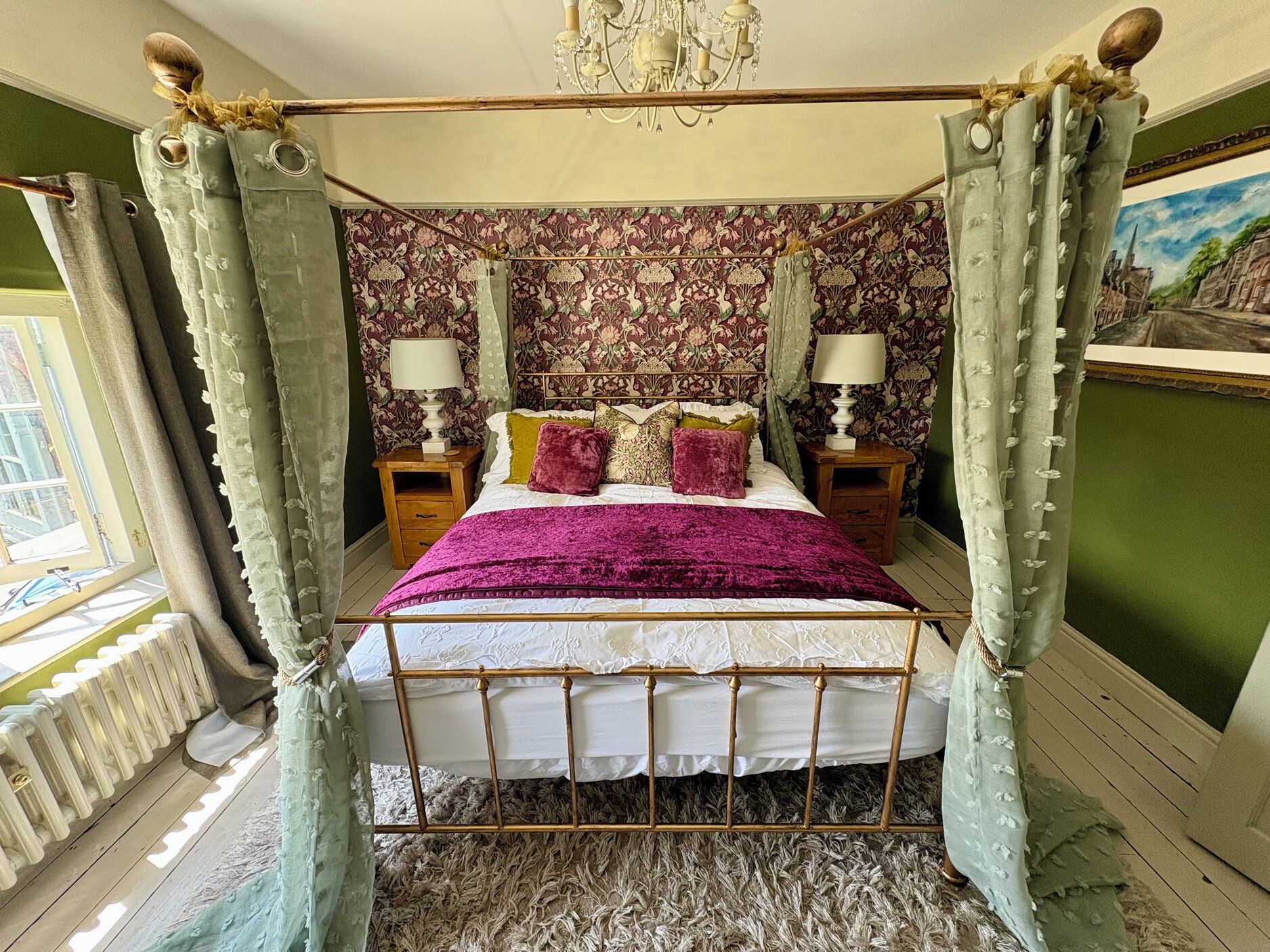 A four-poster bed with a canopy, two bedside tables with lamps, patterned wallpaper, and a painting on the wall.