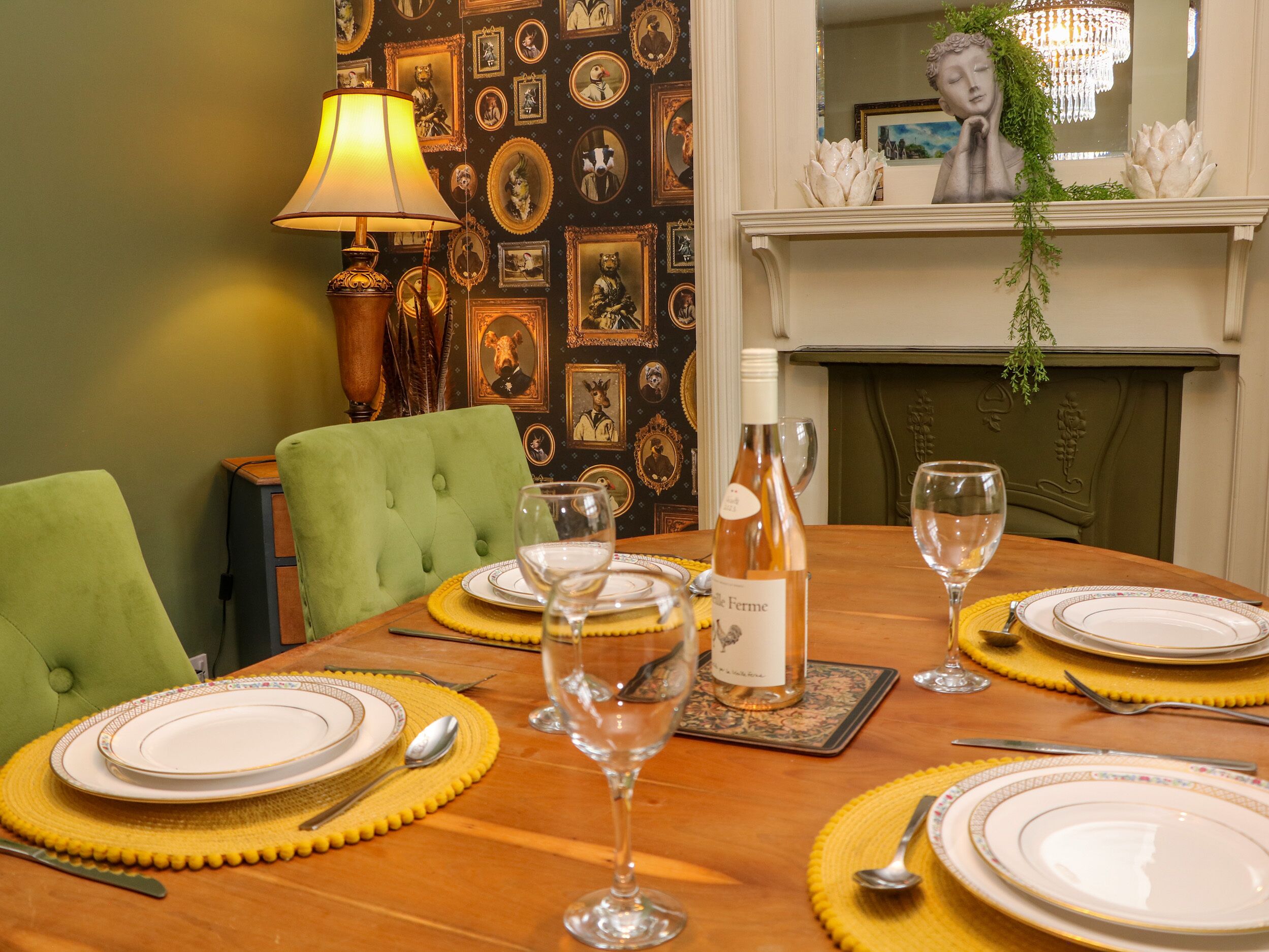 A dining table set with plates, cutlery, and wine glasses, surrounded by green upholstered chairs.