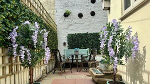 Eine Terrassenfläche mit Tisch und Stühlen, umgeben von Kübelpflanzen und einem Holzzaun.