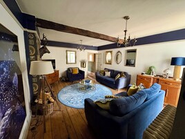 Una sala de estar con un sofá azul, una mesa de centro redonda y una araña.