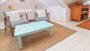 Un dormitorio acogedor en el ático con dos sillones, una mesita, una cama y un armario de madera.