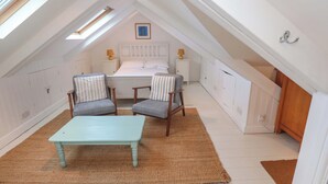 Un dormitorio acogedor en el ático con cama, dos sillones, una mesa y una mesita de noche con lámparas.