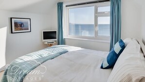A bedroom with a bed, a television, a window with curtains, and a framed picture on the wall. - Dream View (Weymouth)